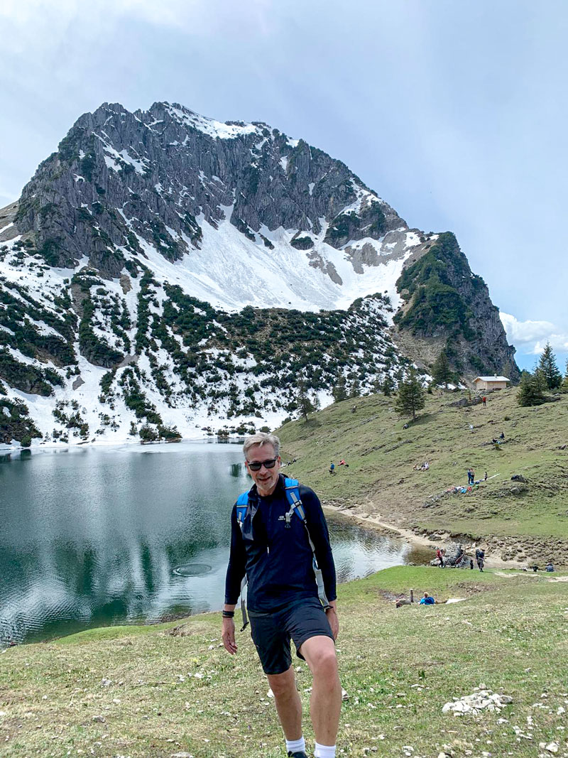 Michael Herzog in den Bergen beim Wandern. Im Hintergrund Berge und See.